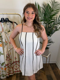 Woman wearing a sleeveless cream dress with black stripes and spaghetti straps in a clothing store.