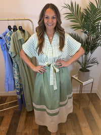 Woman wearing a short sleeve sage and white midi dress with a striped bodice and belt in a clothing store.