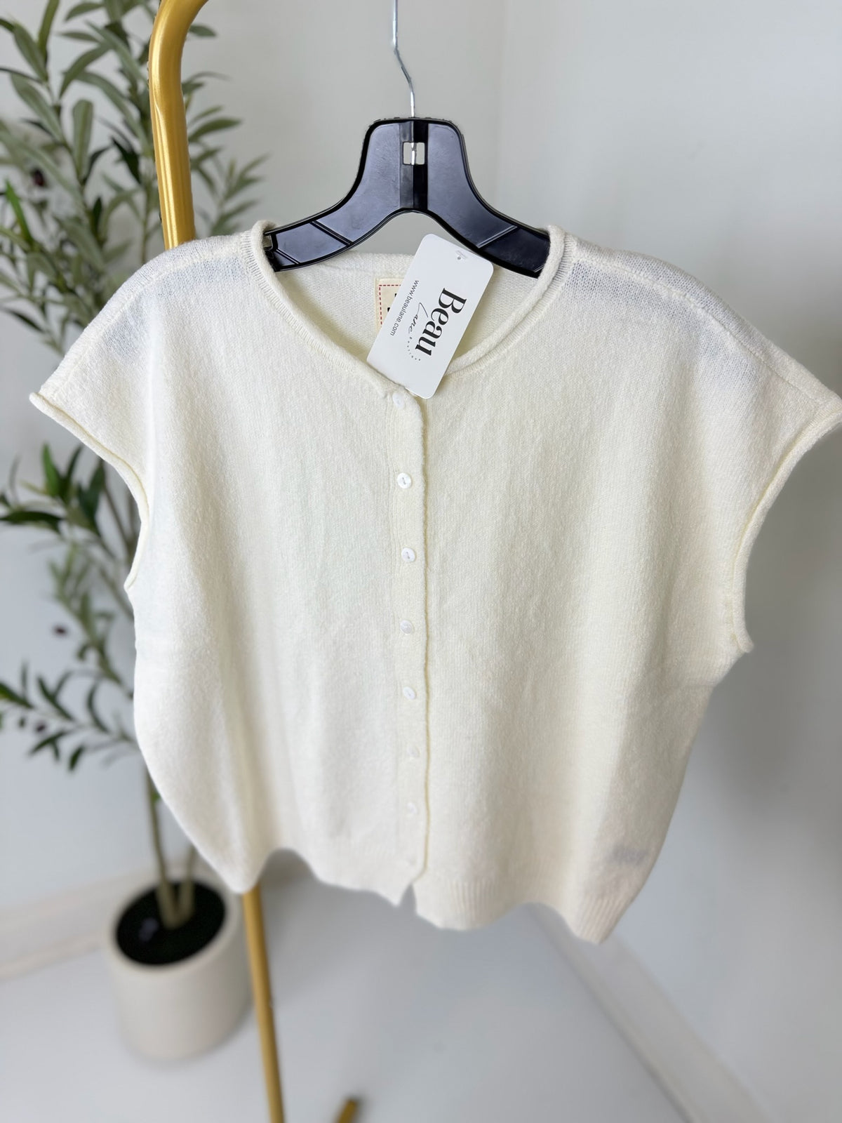 White cardigan on a hanger with a plant in the background