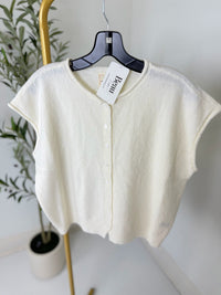 White cardigan on a hanger with a plant in the background