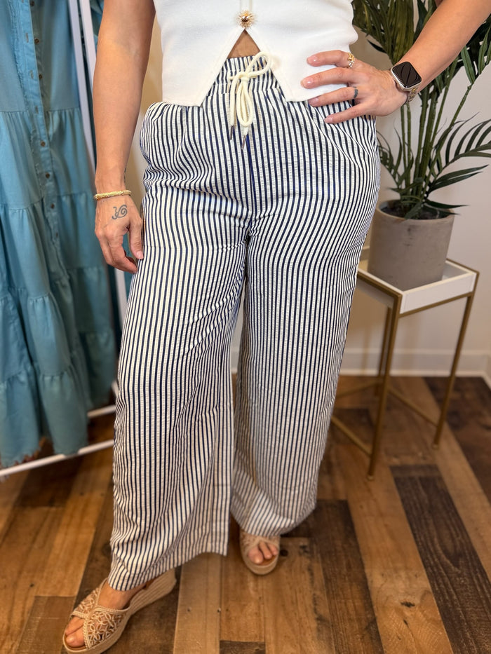 Woman wearing white and navy striped pants with drawstring waist in store setting.