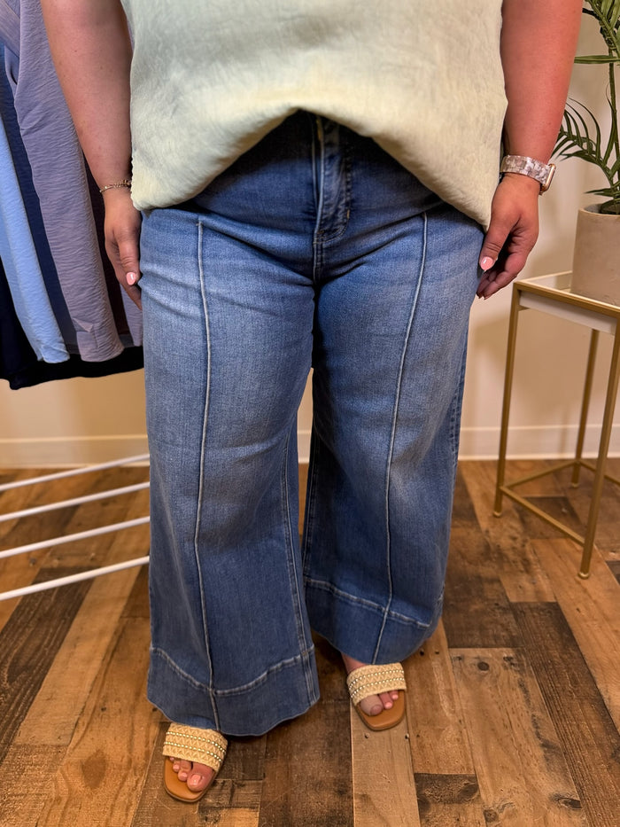 Person wearing wide leg blue jeans with seam detail and a light-colored top in an indoor setting.