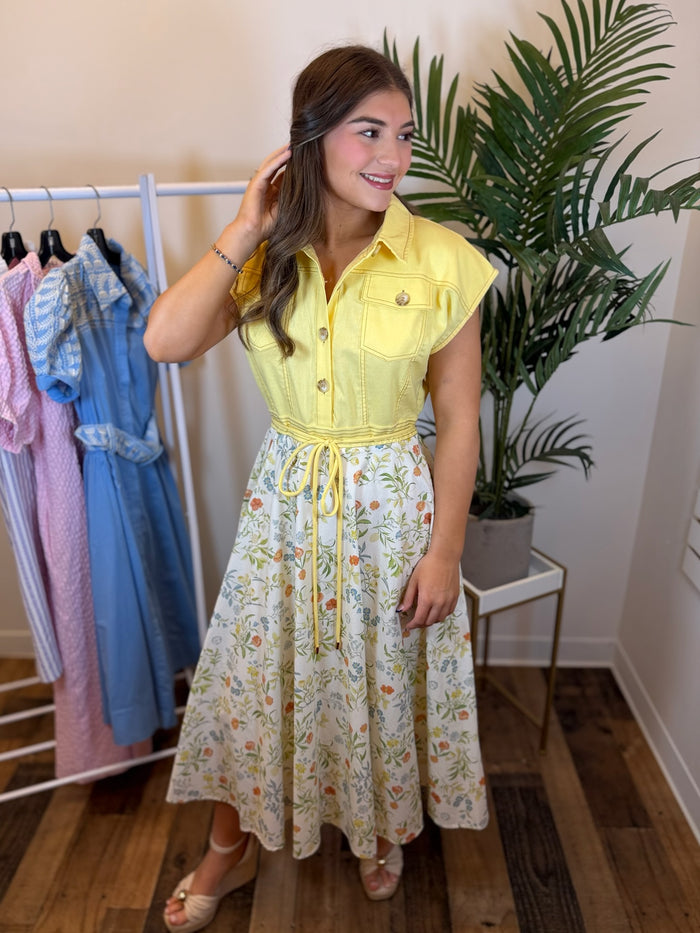 Woman wearing midi dress with yellow bodice and floral skirt in clothing store setting.