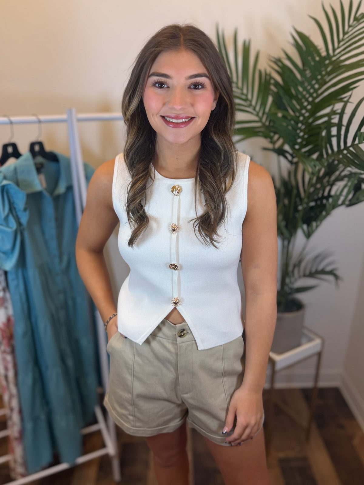 Woman wearing sleeveless white top and khaki shorts in clothing store setting.