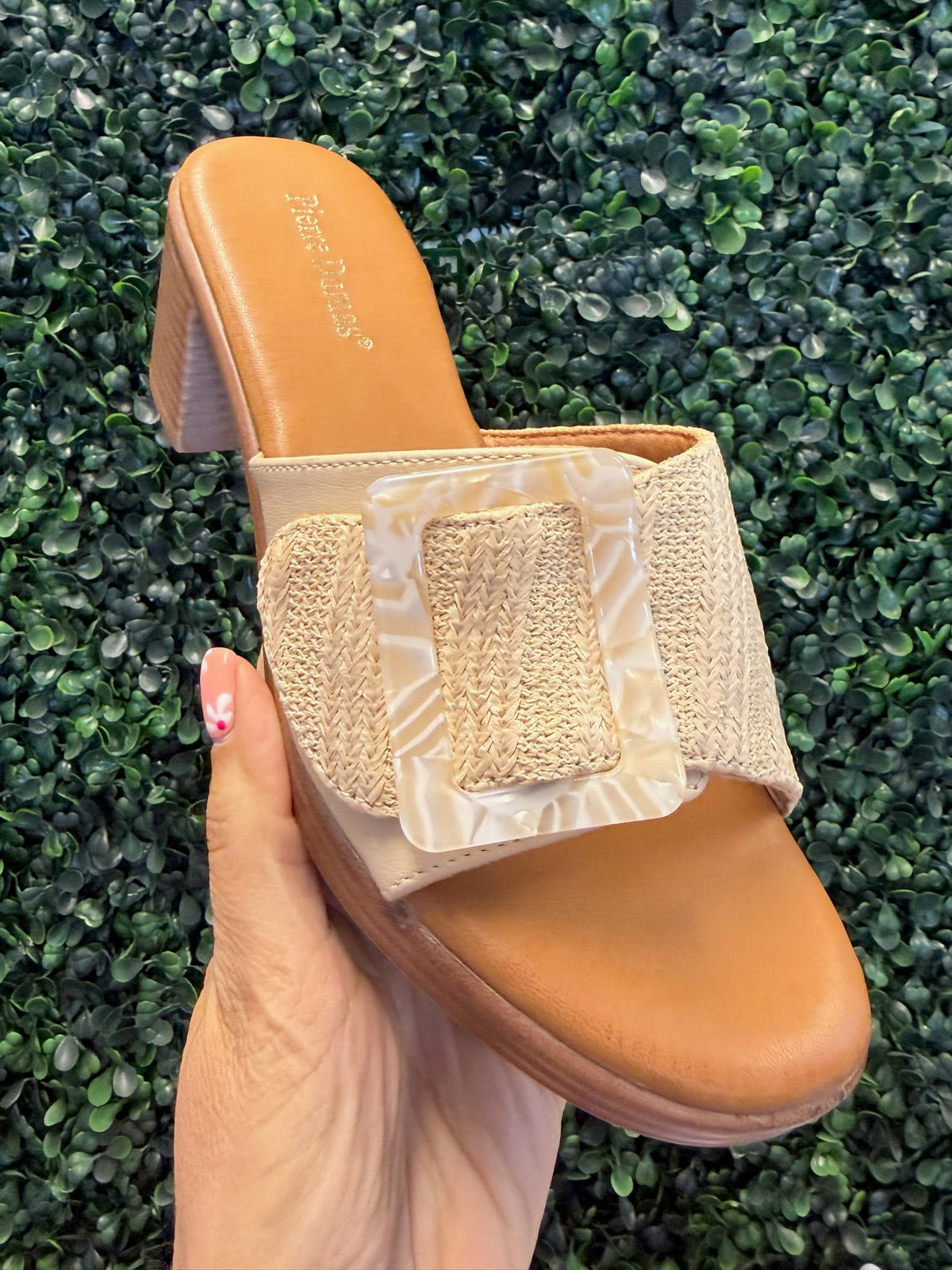 Tan block heel with woven strap held against a green grass background