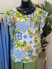 Colorful floral and tropical patterned cap sleeve top in shades of Blue, Yellow, Green, and orange on a hanger with a plant in the background