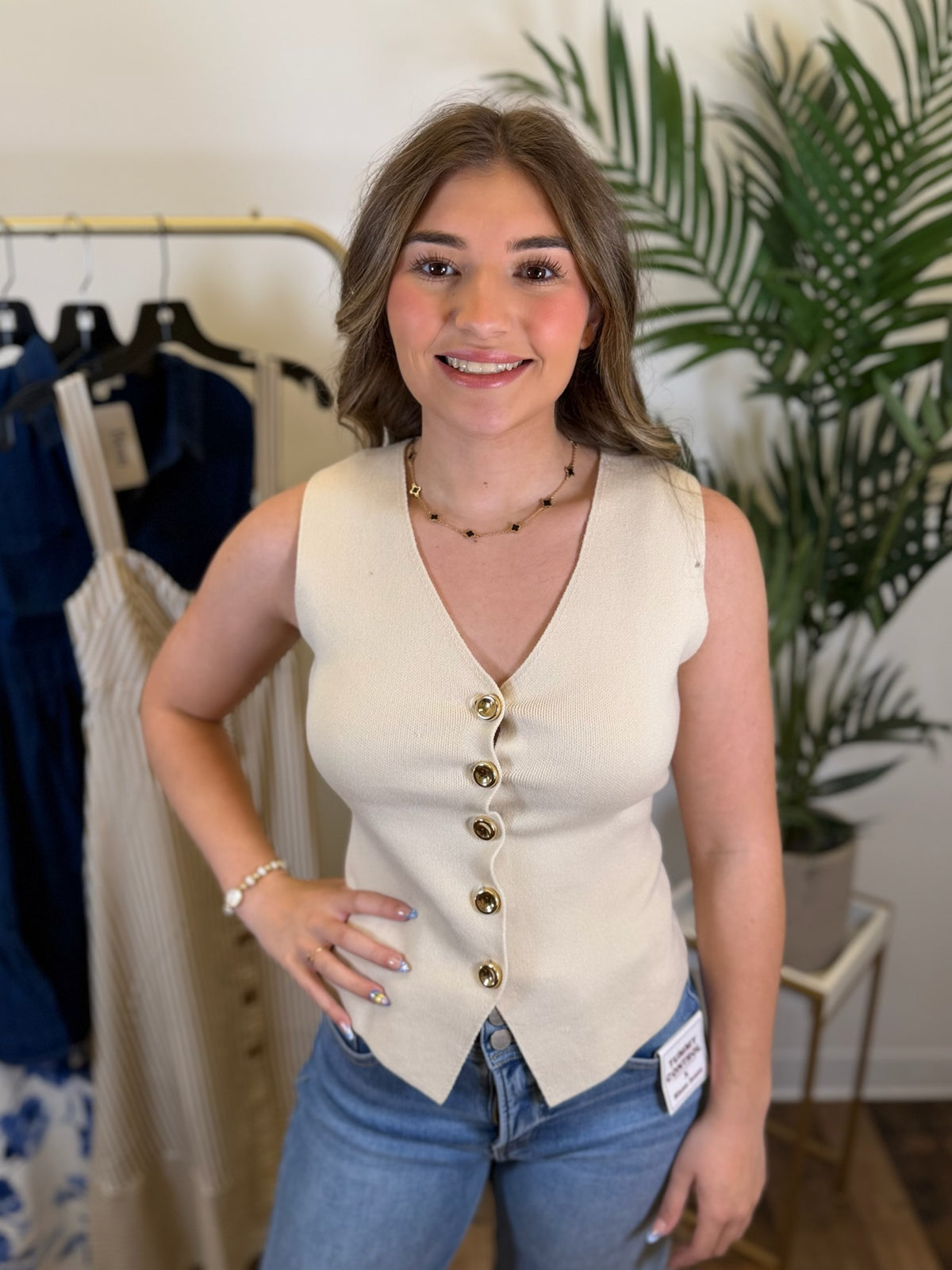 Woman wearing a cream knit vest with jeans, standing in a clothing store.