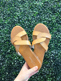 Tan sandals with a visible brand logo held over green grass