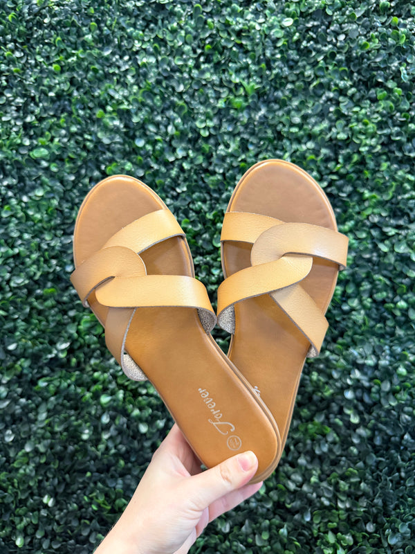 Tan sandals with a visible brand logo held over green grass