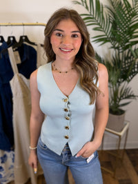 Woman wearing a sleeveless light sage knit vest with gold buttons in a clothing store.