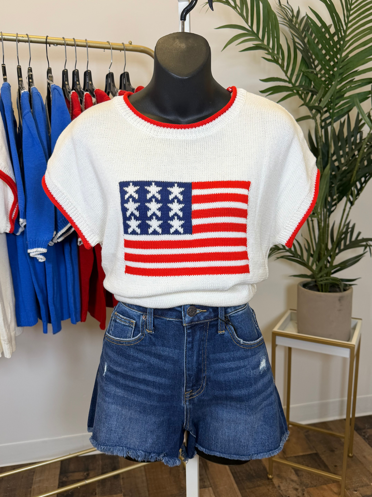 Mannequin wearing a white sweater with American flag design and denim shorts in a store setting.