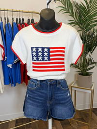 Mannequin wearing a white sweater with American flag design and denim shorts in a store setting.