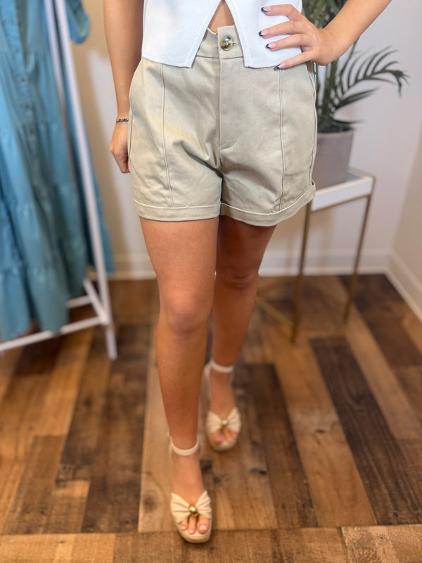 Person wearing tailored khaki shorts with cuffed detail in a clothing store setting.
