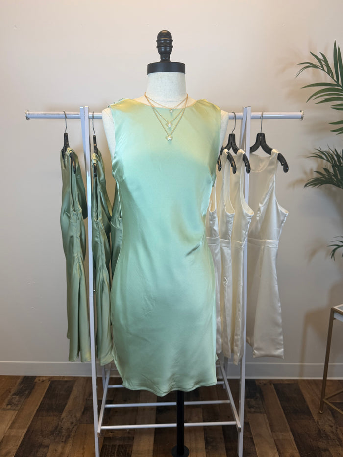 Mannequin wearing a silky light green mini dress with matching dresses on a rack in the background.