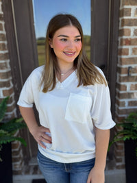 Woman standing against a Brown door wearing a White oversized waffle knit tee with v neck and chest pocket.
