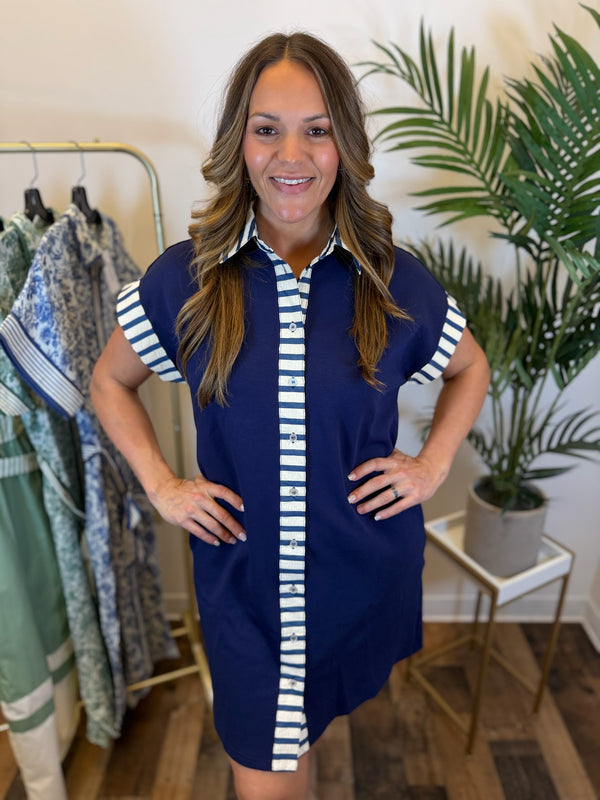 Woman wearing a navy dress with white striped contrast trim details in a clothing store.