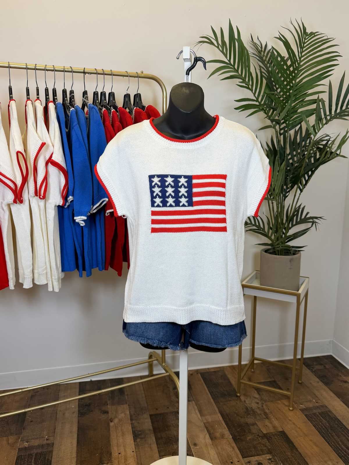 Mannequin wearing a white sweater with an American flag design in a store setting.