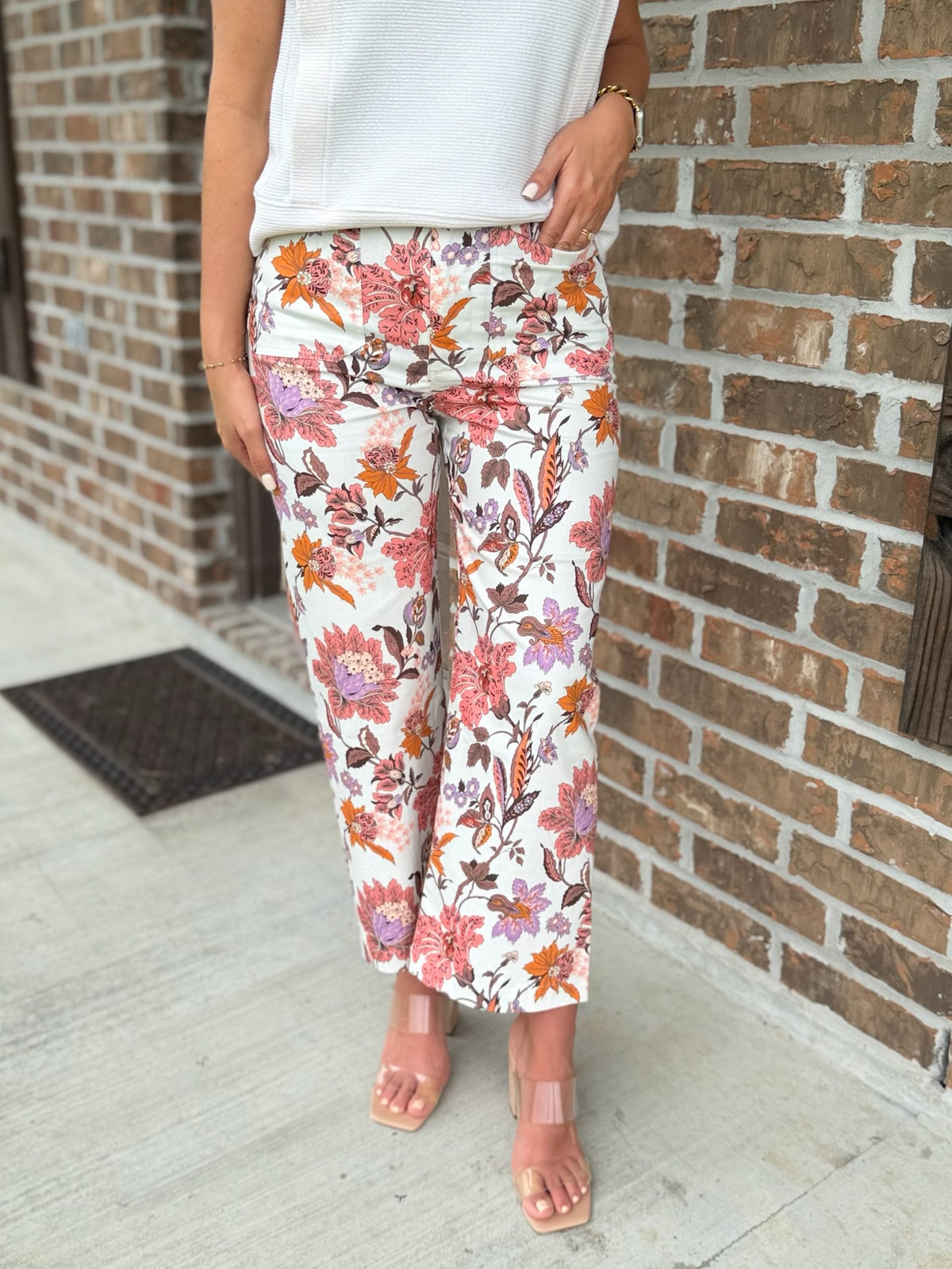 Person wearing wide leg multicolor floral pants standing against a brick wall.