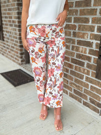 Person wearing wide leg multicolor floral pants standing against a brick wall.