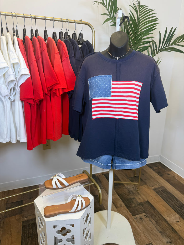 Navy blue vintage wash t-shirt with American flag design on a mannequin, surrounded by colorful shirts on hangers.