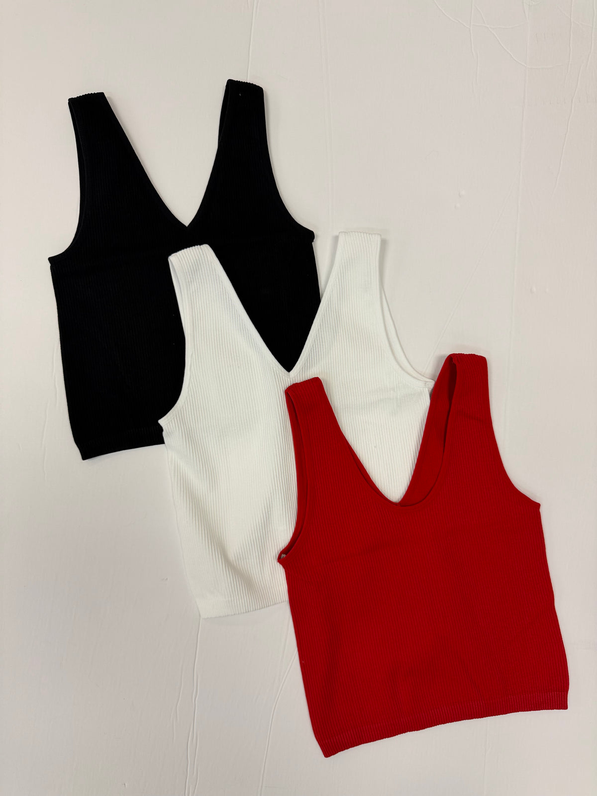 Red, white, and black sleeveless v neck crop tops on a white background