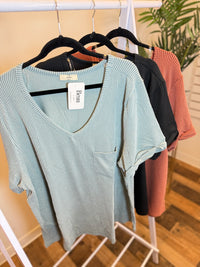 Light blue ribbed v-neck top with rolled sleeves and pocket, alongside black and terracotta versions.