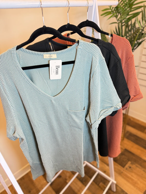 Light blue ribbed v-neck top with rolled sleeves and pocket, alongside black and terracotta versions.