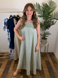 Woman wearing a light green and off white striped maxi dress in a room with clothing racks and plants