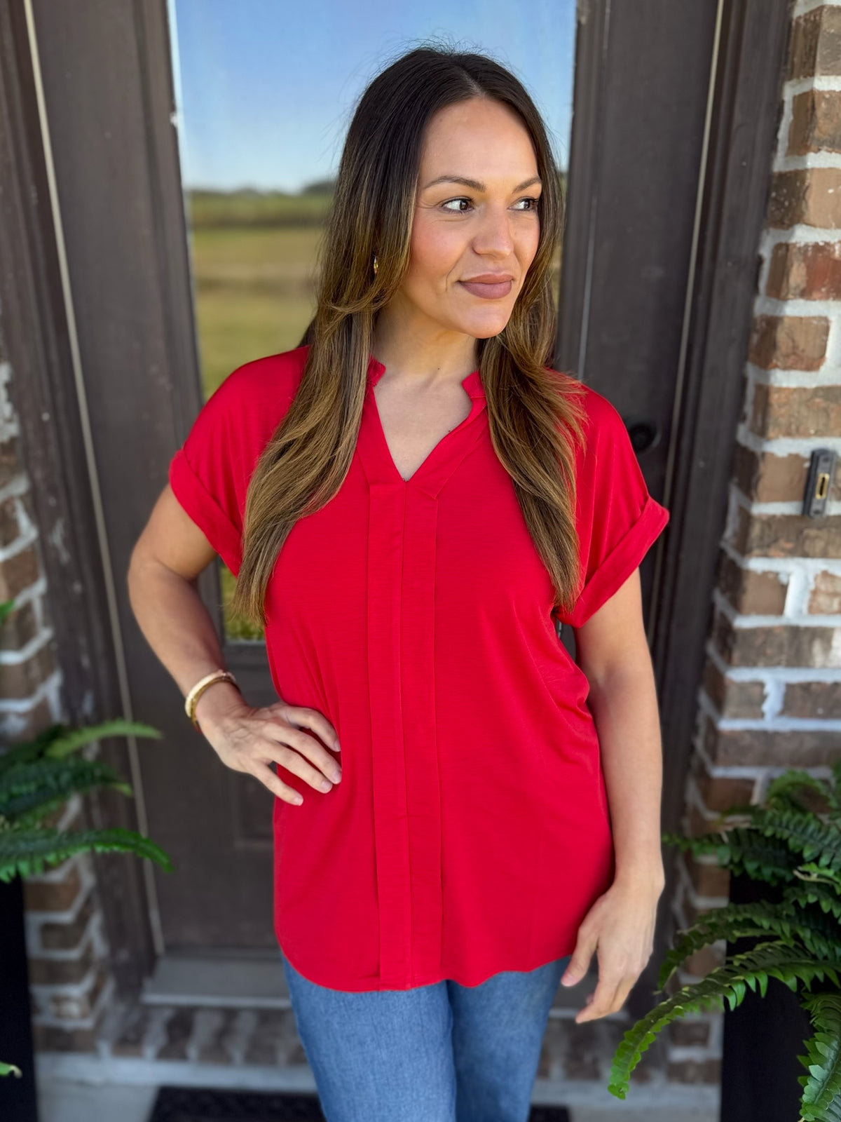 Woman wearing a red short sleeve blouse with a split V-neckline paired with jeans, standing outdoors.
