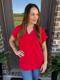 Woman wearing a red short sleeve blouse with a split V-neckline paired with jeans, standing outdoors.