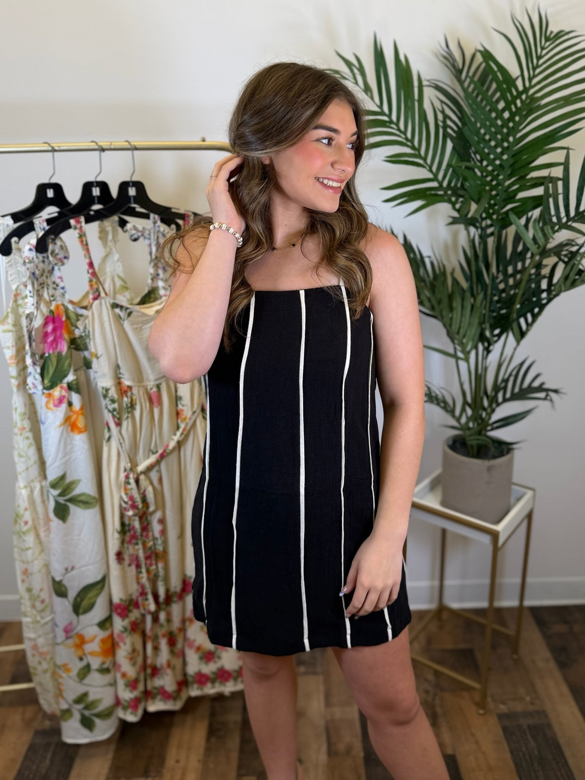 Woman wearing a sleeveless black dress with white stripes in a clothing store.