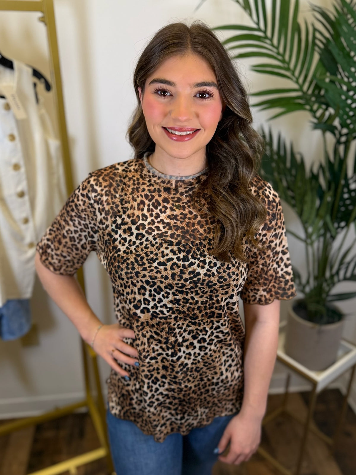 Person wearing a mesh leopard print top with short sleeves and ruffled trim in a room with plants and clothing racks.