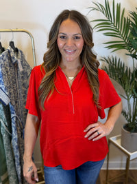 Woman wearing a red blouse with short sleeves and collared v neck with scalloped trim in a clothing store setting
