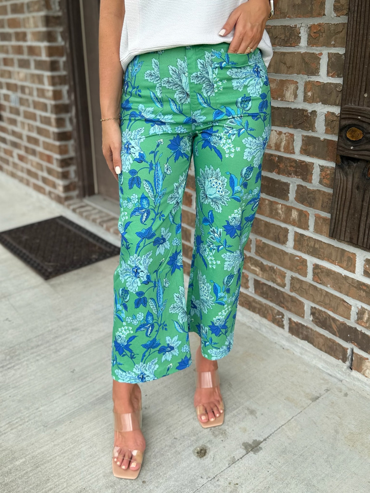 Person wearing green wide leg floral pants standing in front of a brick wall.