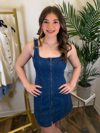 Woman wearing a blue denim dress in a room with plants and clothing racks.