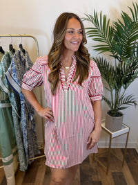 Woman wearing a red and white striped dress with split neckline and puff sleeves in a clothing store.