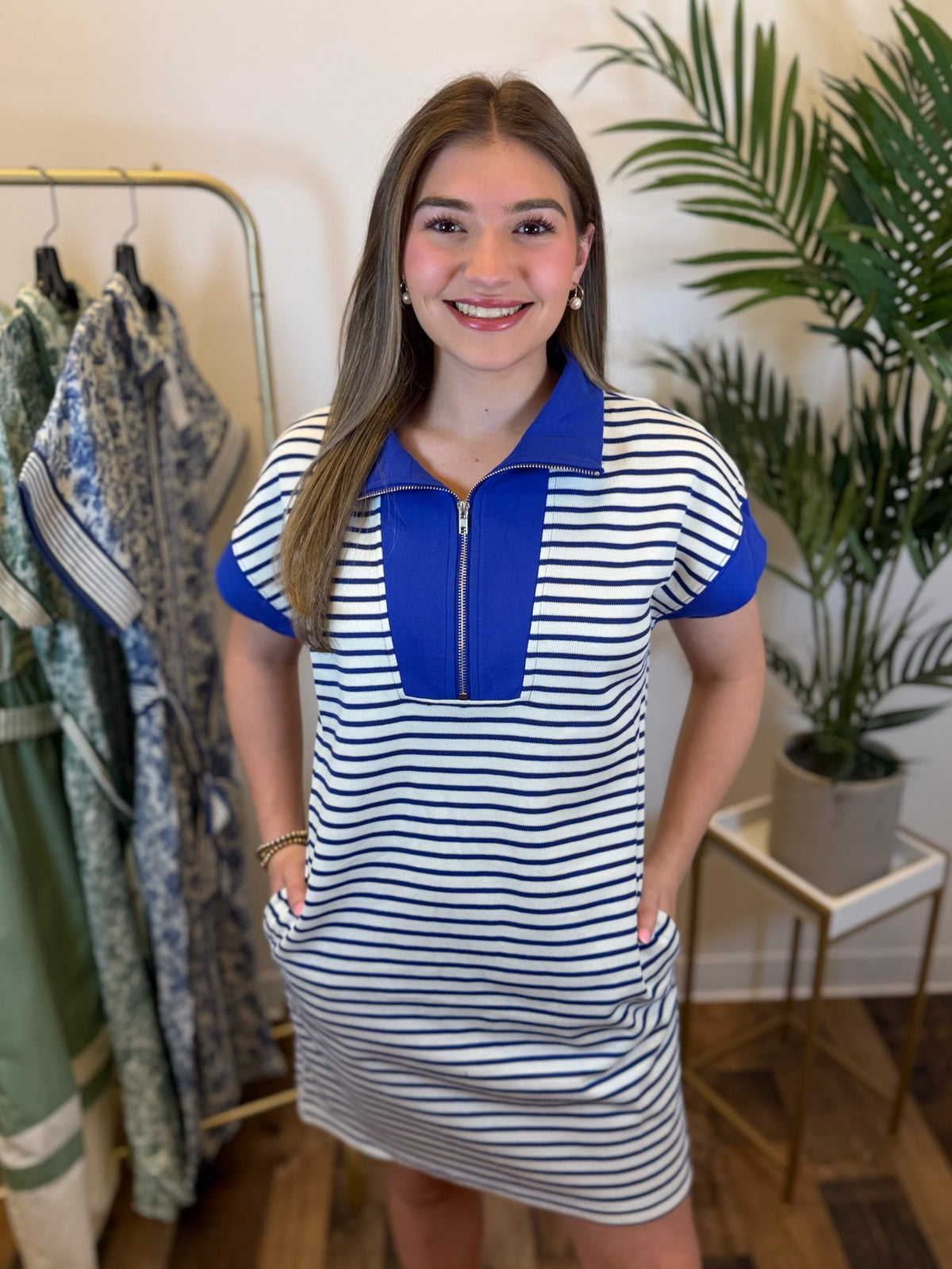 Woman wearing a short sleeve royal blue and white striped dress with a zipper and blue contrast trim details in a clothing store.