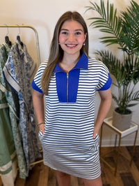 Woman wearing a short sleeve royal blue and white striped dress with a zipper and blue contrast trim details in a clothing store.