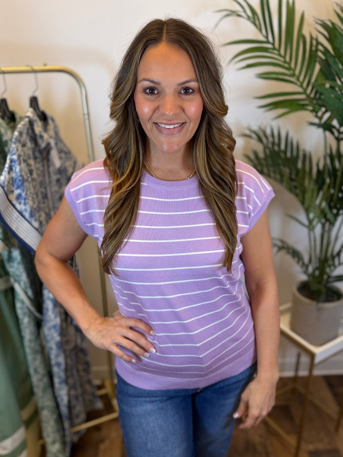 Woman wearing a short sleeve knit purple shirt with white horizontal striped print in a clothing store setting