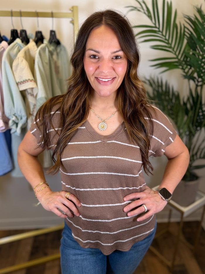 Woman wearing a brown striped shirt and blue jeans in a clothing store.