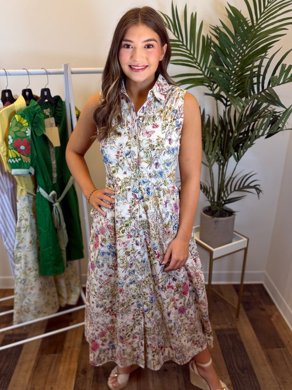 Woman wearing sleeveless cream floral dress with button front and collar standing in clothing store setting.