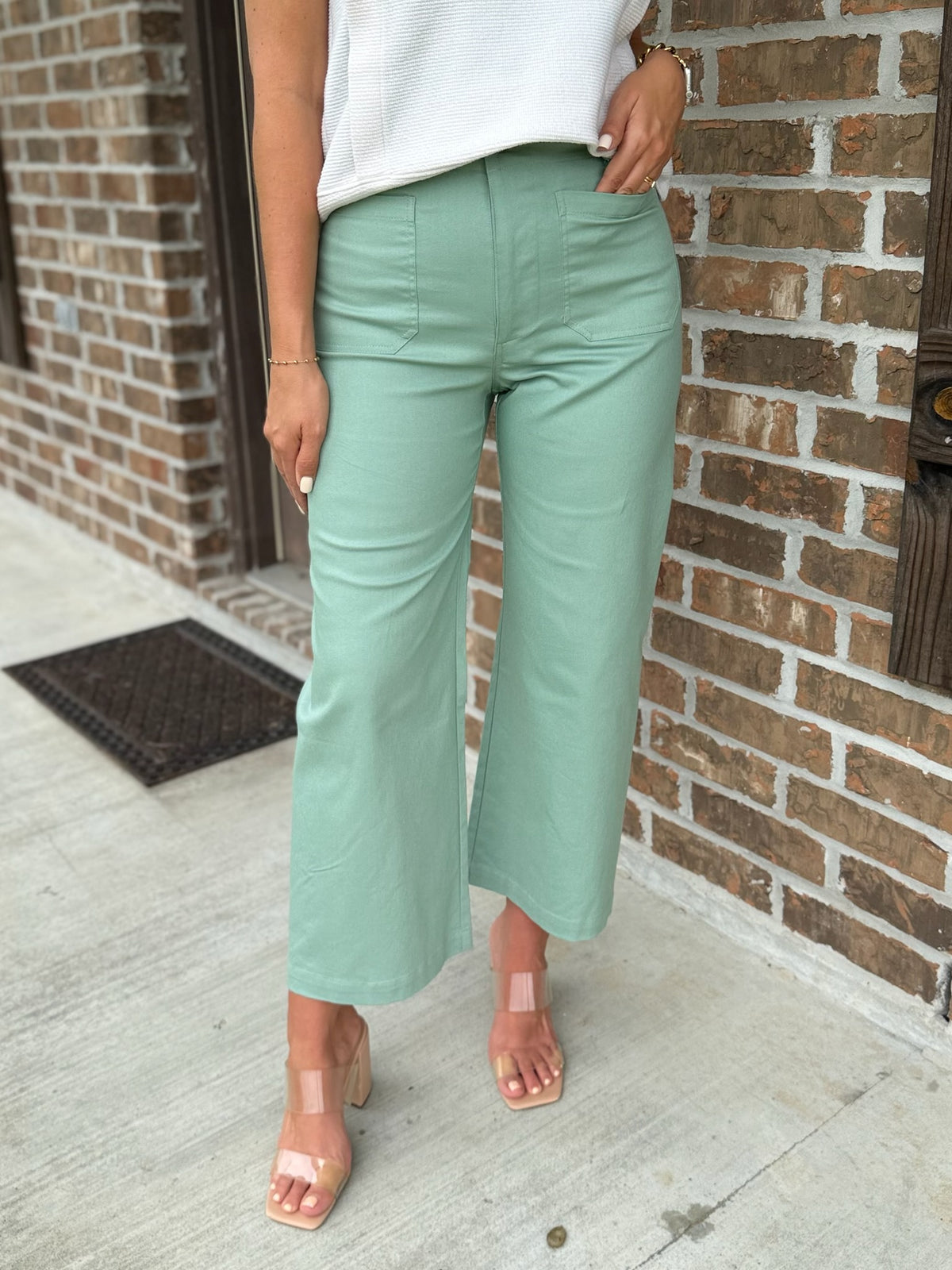 Person wearing light green cropped pants with functional front pockets standing against a brick wall.