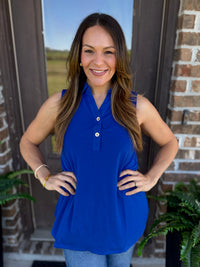 A woman wearing a sleeveless royal blue polo-style top with a three-button placket, standing in front of a brick doorway.