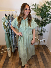 Woman wearing a green and white striped maxi dress in a clothing store.