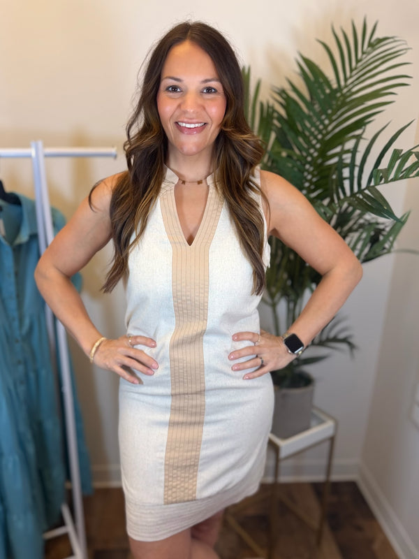 Woman wearing a cream and beige dress in a room with plants and clothing racks.