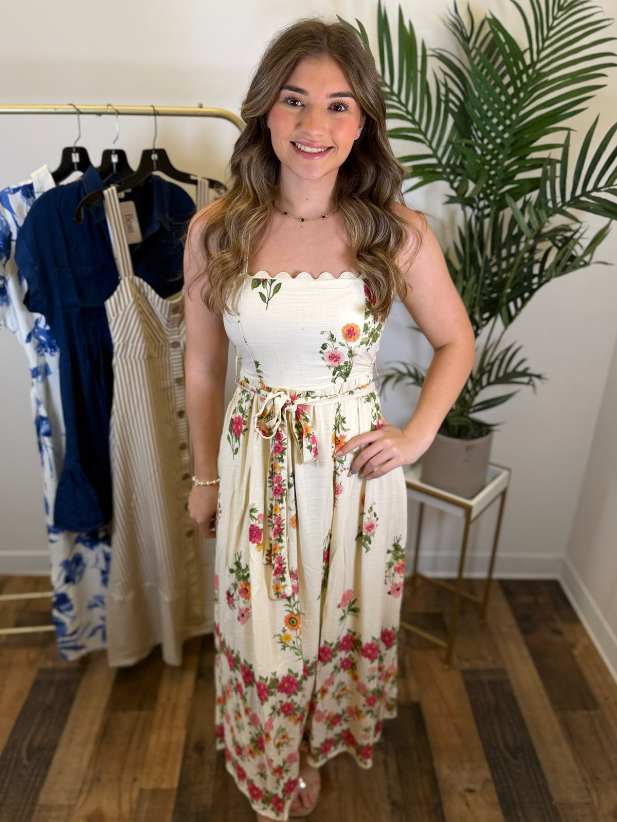 Woman wearing a floral dress standing in a room with clothing racks and plants.