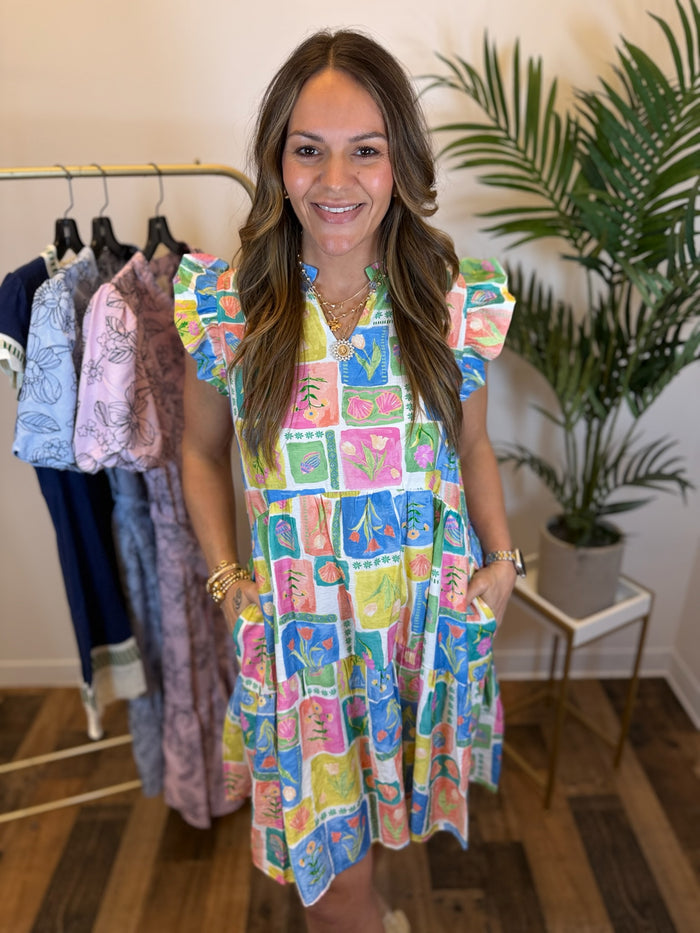 Woman wearing a bright and colorful patterned dress with ruffled sleeves and split neckline in a clothing store.