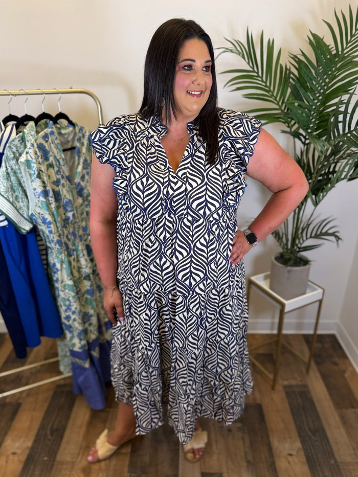 Woman wearing a navy and cream patterned midi dress with split neckline and ruffled cap sleeves in a clothing store.