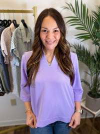 Woman wearing a purple shirt in a clothing store with plants in the background