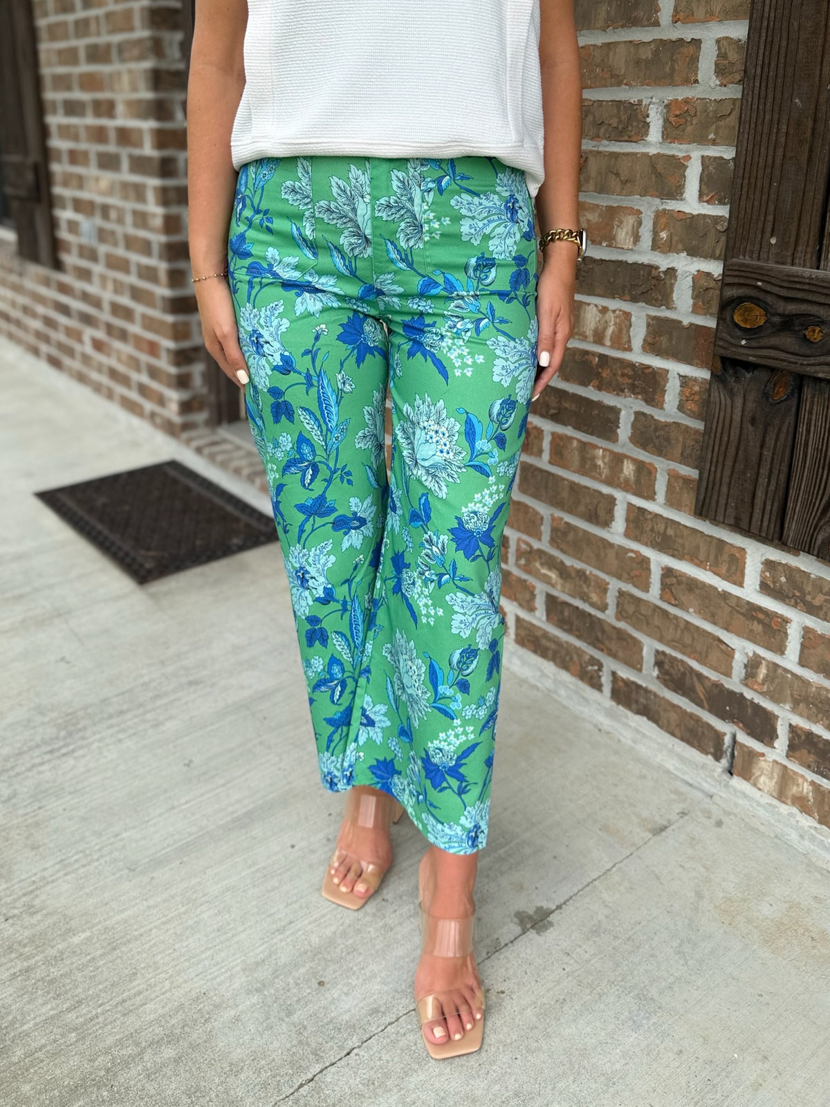 Person wearing green pants with blue floral accents standing in front of a brick wall.